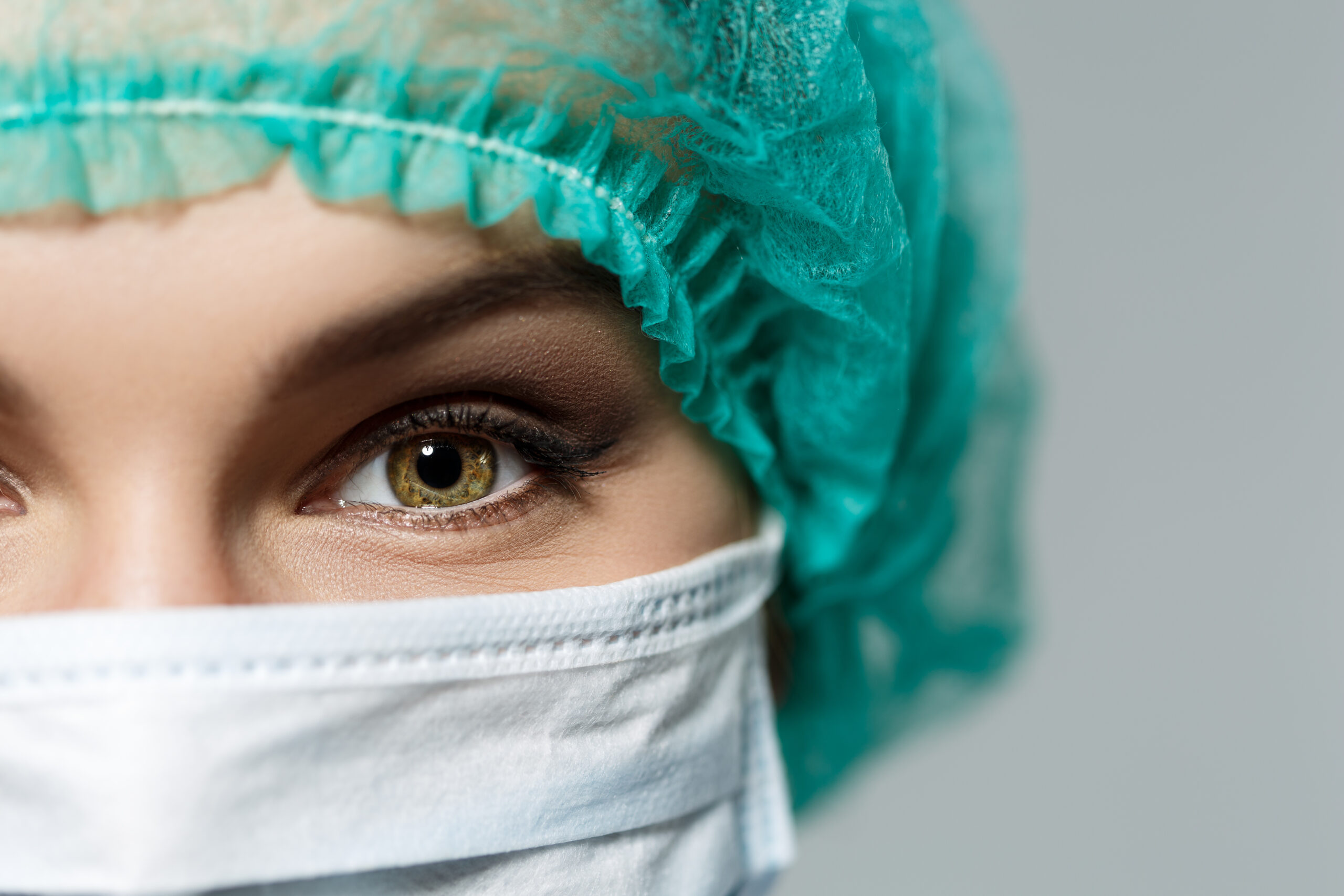 Female doctor's face wearing protective mask and green surgeon's cap closeup. Surgeon's eyes close up gazing intently in camera. Resuscitation concept.