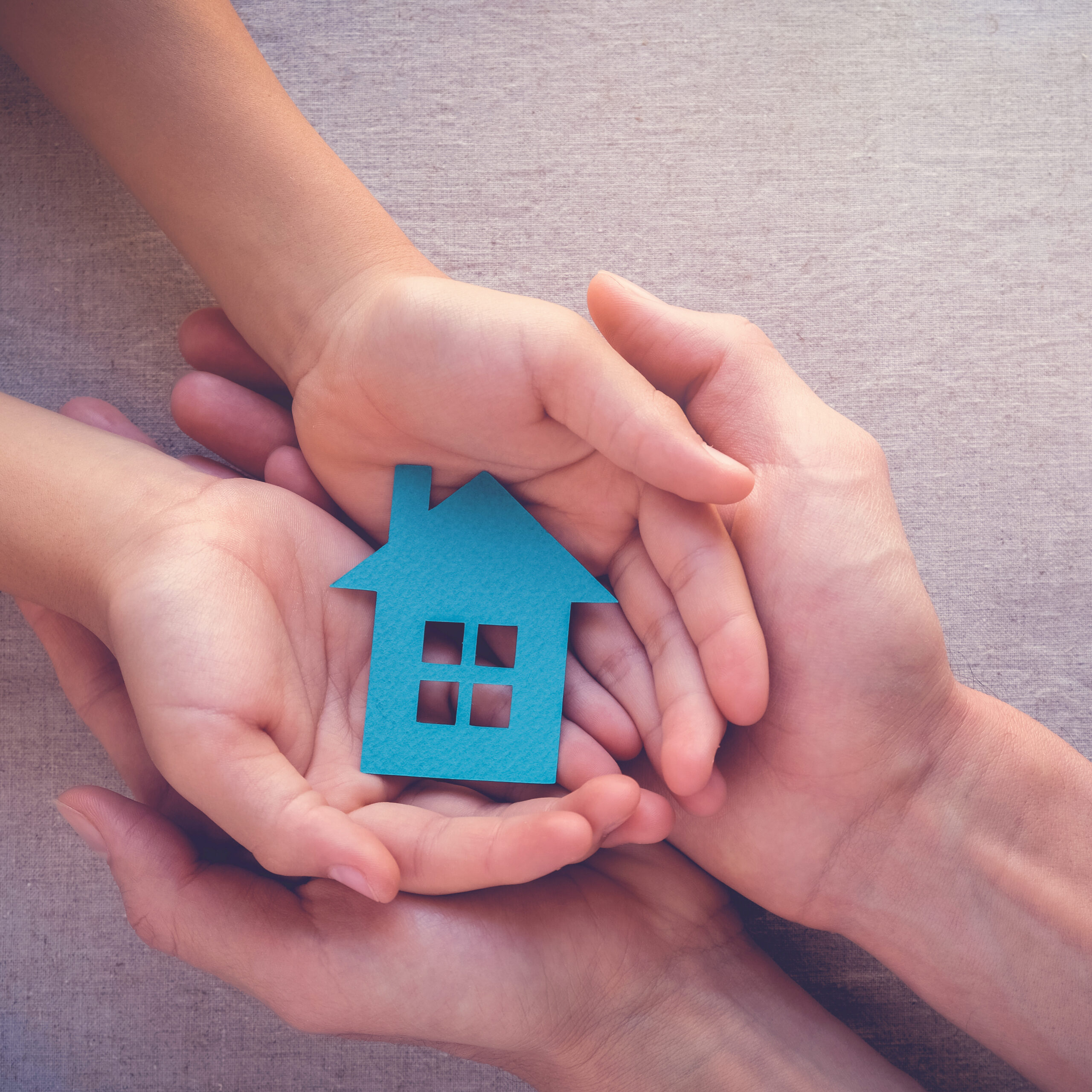 Adult and child hands holding paper house, family home, homeless shelter and real estate concept