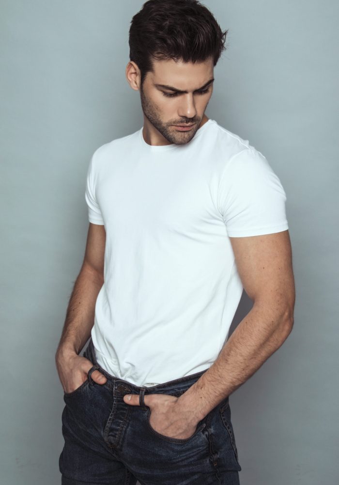 Muscle strong beautiful stripped male model in denim blue jeans with white t-shirt on grey isolated font background Muscle strong beautiful stripped male model in denim blue jeans with white t-shirt on grey isolated font background