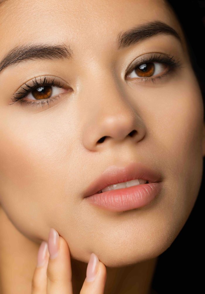 Close-up cropped image of beautiful female with plump lips touching her face isolated on brown studio background. Concept of female beauty and tenderness