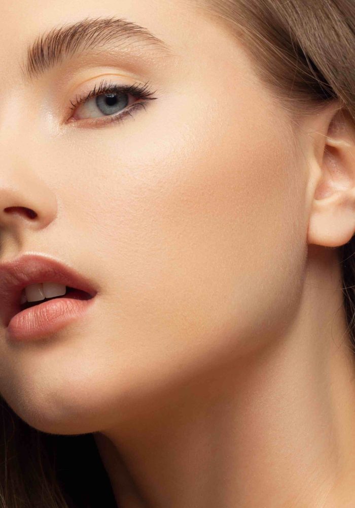 Close up beauty of a half face of a woman with wet radiant skin and big gray eyes. Fashionable natural makeup and wet facial hair. Nude lipstick with kissed lips