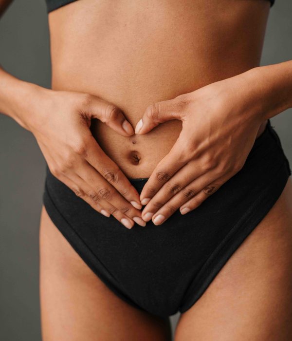 Close up off African American female standing and making a heart shape with her hands on her tummy. High quality photo