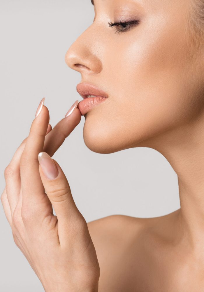 Lip augmentation. Beautiful girl touching her lips over gray background, copy space