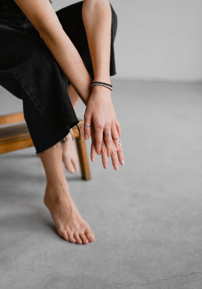 Partial view of barefoot woman in dark jeans touching hands near step stool on grey