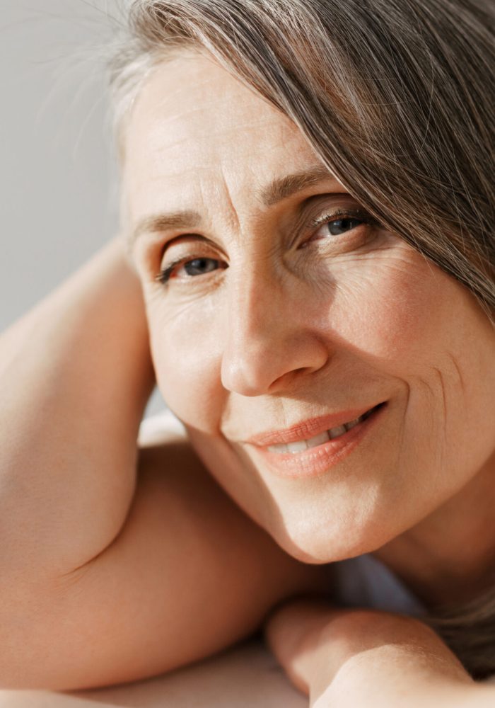 Grey senior woman in t-shirt smiling and looking at camera isolated over white background