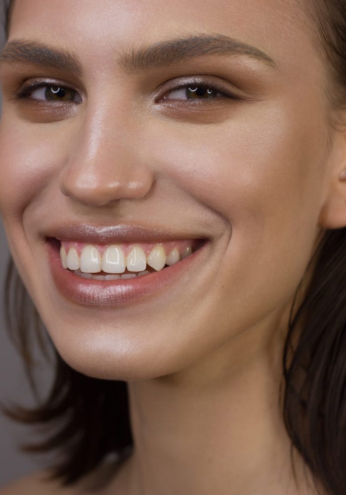 Close-up portrait of the cleanliness face of a beautiful woman with dark black smoky eyes makeup, natural full lips. Sexy model with clean shiny skin, clean face, long curly hair. snow-white smile