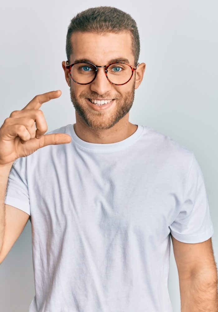 Young caucasian man wearing casual clothes and glasses smiling and confident gesturing with hand doing small size sign with fingers looking and the camera. measure concept.