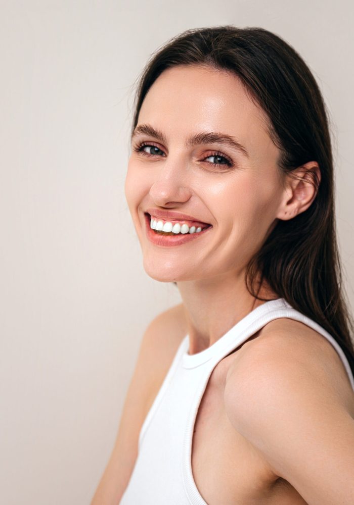 portrait of happy woman with healthy radiant skin and natural makeup looking at camera. model posing on copy space beige background. beauty procedure and skincare concept