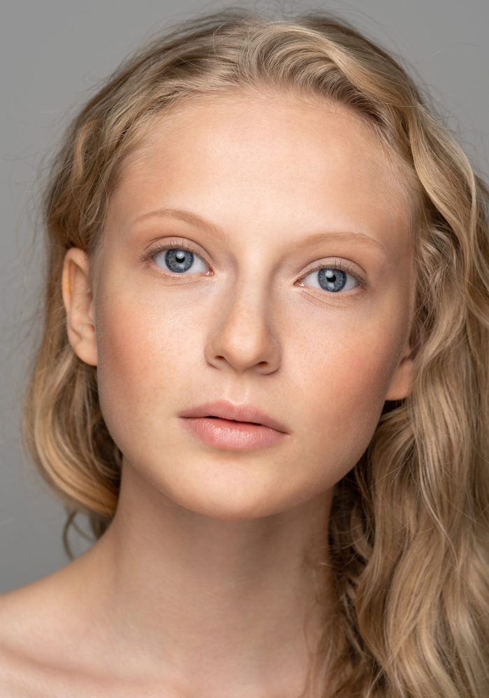 Close up of young woman face with blue eyes, curly natural blond